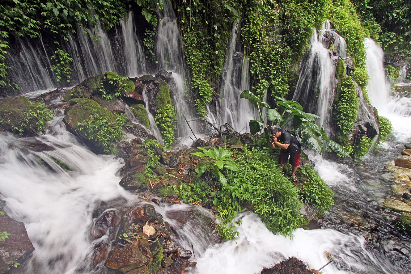 SEGERA BERAKHIR: Seorang warga memotret air terjun di Sumber Pitu, Kecamatan Tumpang, Kabupaten Malang. (suharto/radar malang)