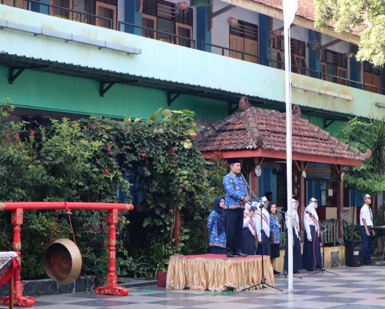 BERI MOTIVASI: Kadisdikbud Kota Malang Suwarjana SE MM (berdiri) hadir memimpin upacara sekaligus memukul gong pertanda dibukanya MPLS di SMPN 6 Malang, kemarin (17/7).