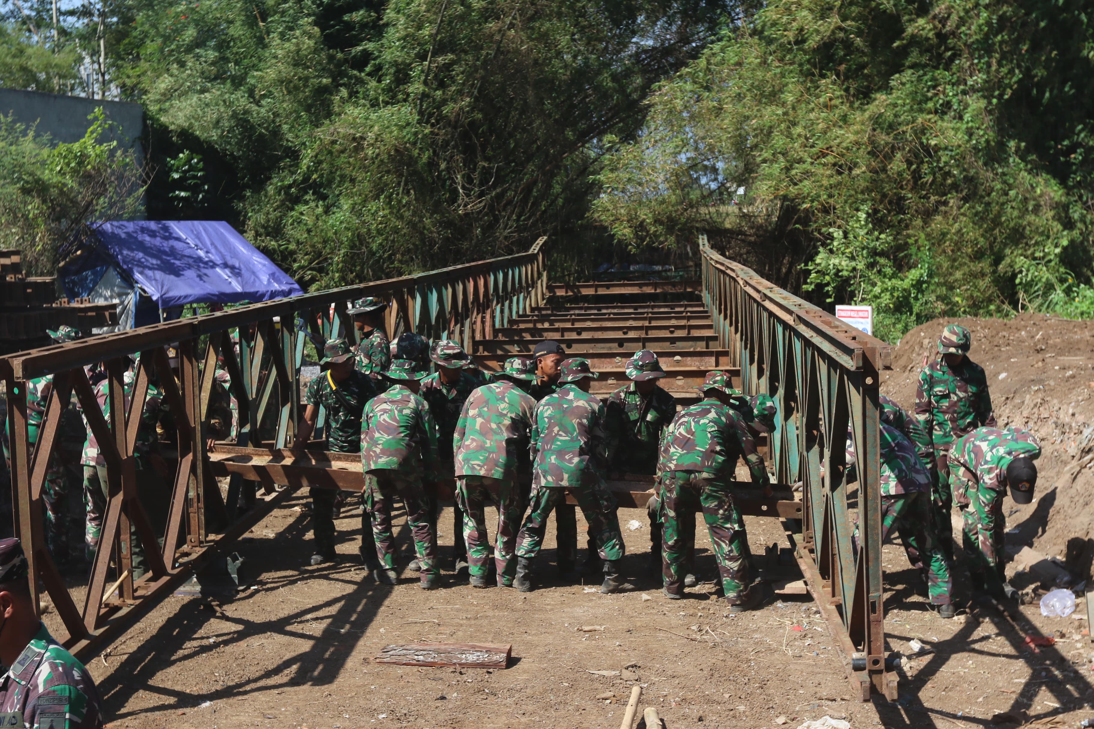 KOKOH: Puluhan prajurit dari Batalyon Zeni Tempur 5 membangun jembatan bailey atau baja di Pandanwangi, Kecamatan Blimbing kemarin (19/7)