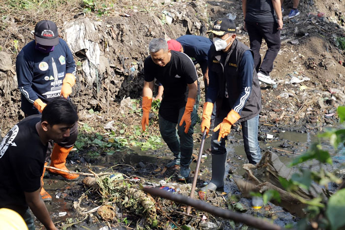 Pj Wali Kota Malang Wahyu Hidayat mencangkul sedimen dan sampah untuk dikeluarkan dari sungai.