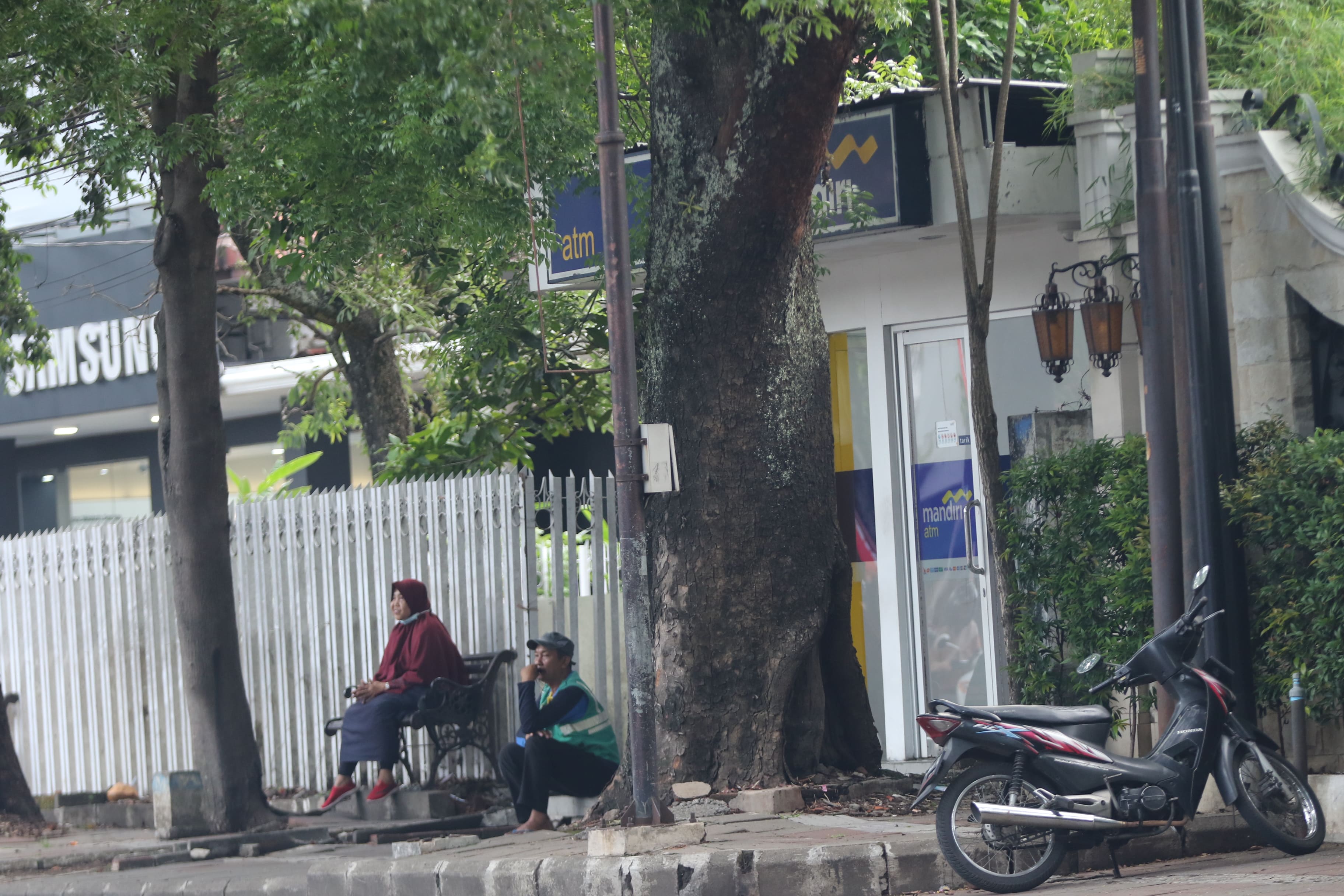 BAKAL DITERTIBKAN: Seorang jukir duduk di depan ATM kawasan Jalan Ijen kemarin (26/11). Dia akan memungut uang kepada setiap kendaraan yang parkir.