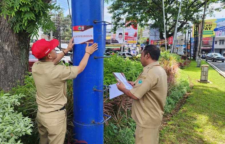 PELANGGARAN: Dua petugas Disnaker-PMPTSP Kota Malang memberi stiker khusus ke salah satu reklame tak berizin di kawasan Jalan Veteran. (Disnaker-PMPTSP Kota Malang for Radar Malang)