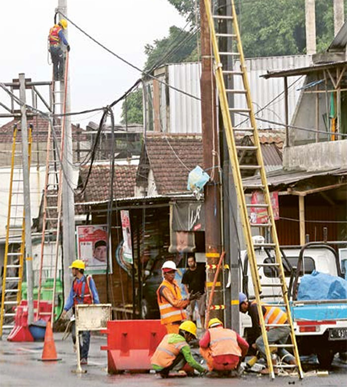 PERALATAN LENGKAP: Beberapa personel  dari PLN memindahkan tiang listrik yang  berada di tengah ruas jalan kawasan Jalan  Ki Ageng Gribig kemarin (10/1).