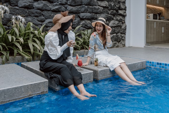 Dua pengunjung wanita mencoba villa dengan kolam renang air hangat di Rayz Hotel UMM