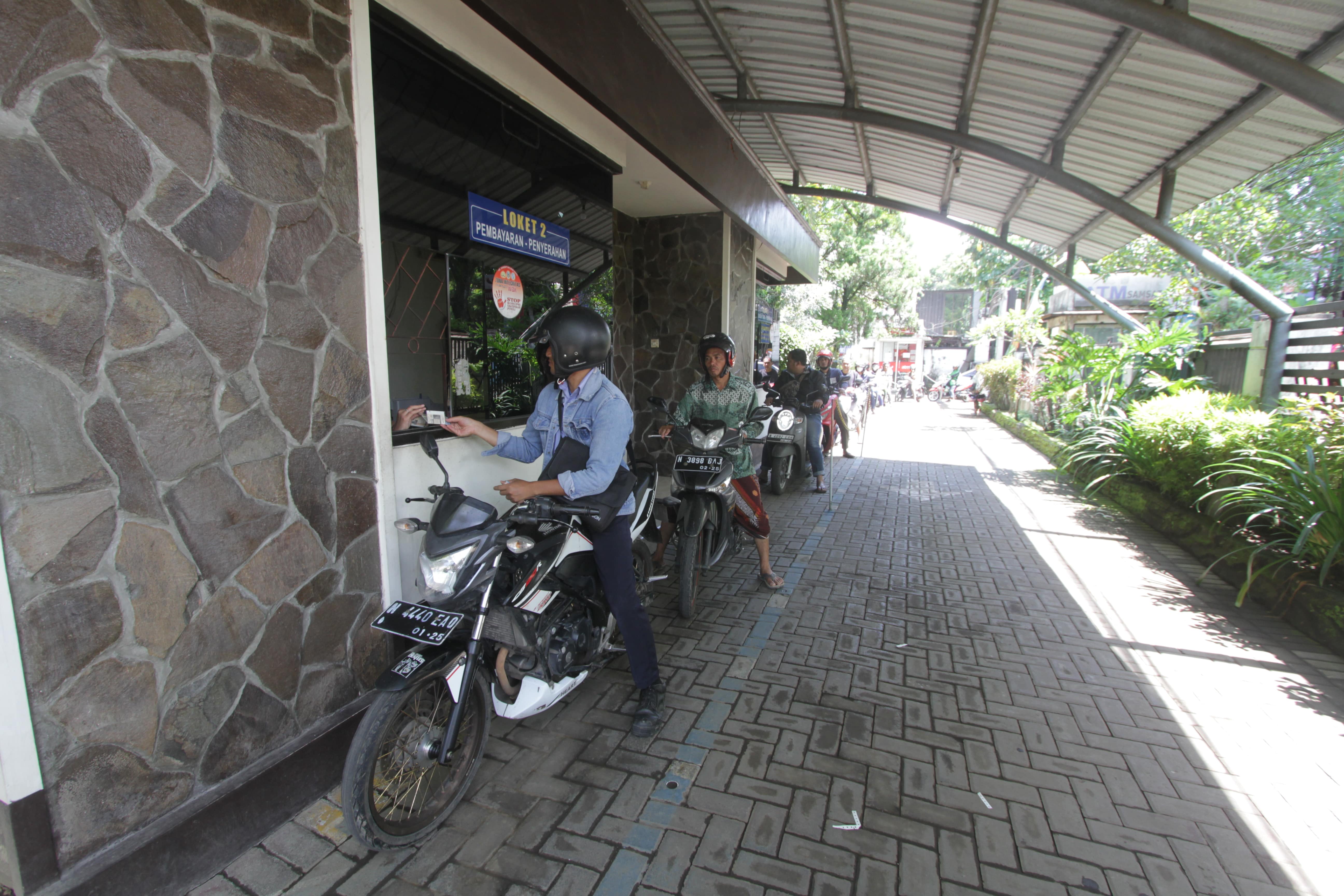 MENGULAR: Pengendara yang mengurus administrasi kendaraan mengantre hingga pintu utama kemarin.