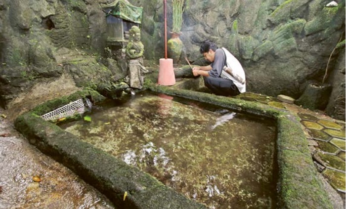 TRADISI: Dika Maulana memasang dupa di Sumber Kamulyan yang berada di sebelah timur Candi Sumberawan, Desa Toyomarto, Kecamatan Singosari, Kabupaten Malang.