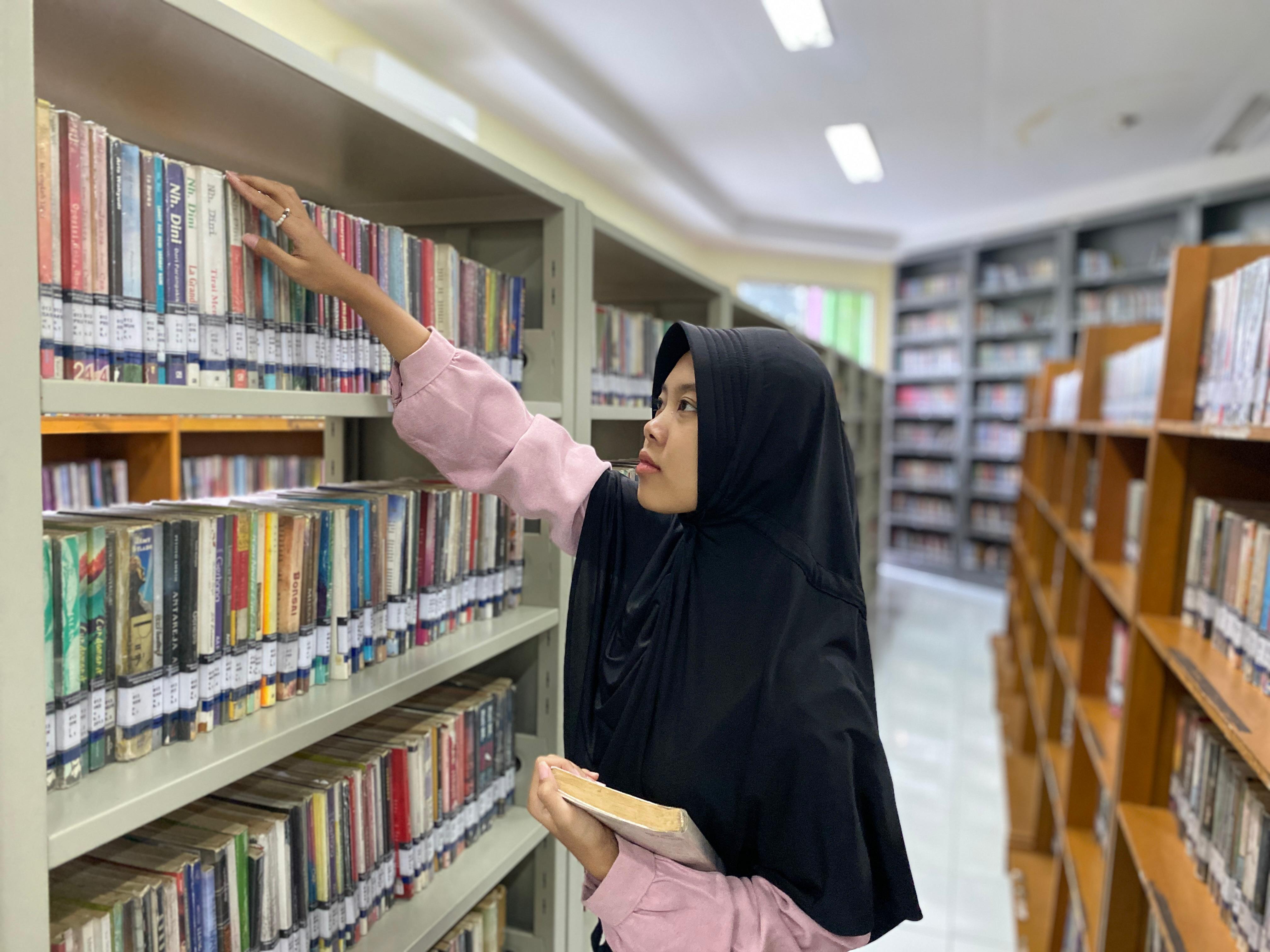 RAMAI KUNJUNGAN: Seorang pengunjung memilih buku yang terpajang di rak perpustakaan kemarin. Mereka terbiasa membaca buku sambil menunggu waktu berbuka.