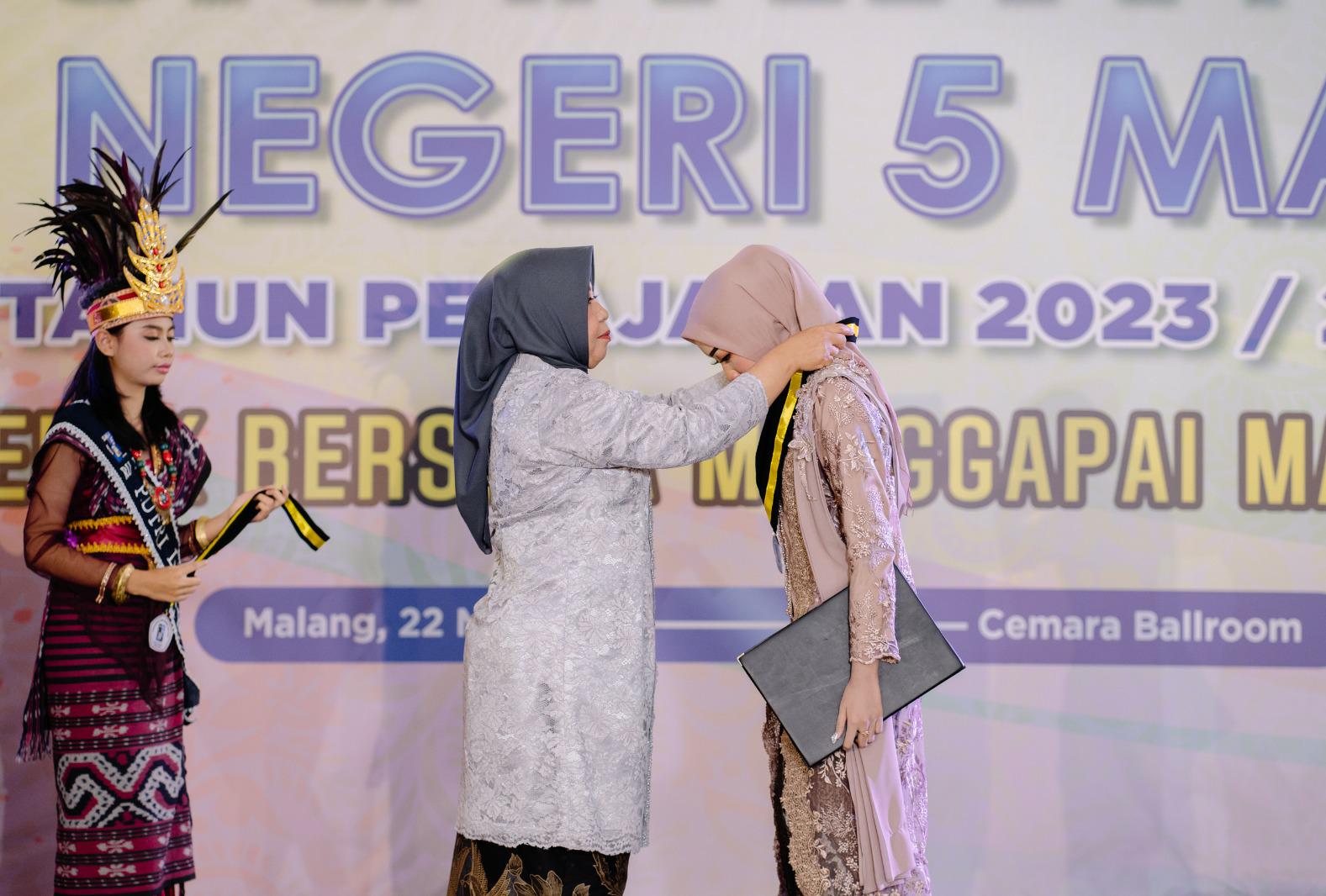 MOMEN HARU : Kepala Sekolah Hj Asri Widiapsari MPd (tengah) menyematkan tanda Purnawiyata kepada salah satu siswi SMAN 5 Malang.