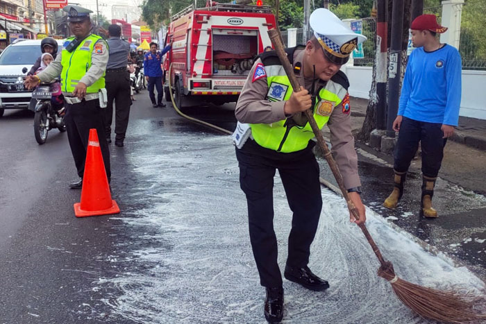 LICIN: Polisi dan petugas BPBD Kota Malang membersihkan tumpahan minyak goreng di Jalan Raya Landungsari kemarin (11/6).