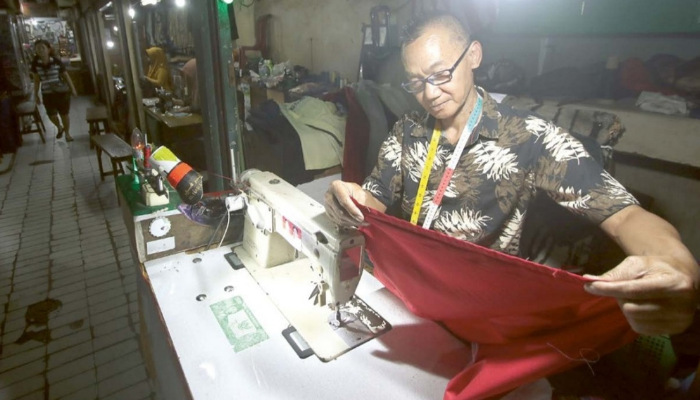 satria cahyono/radar malang  TETAP BERTAHAN: Salah satu penjahit di Pasar Besar Malang menyelesaikan pesanan seragam sekolah kemarin siang (8/7).