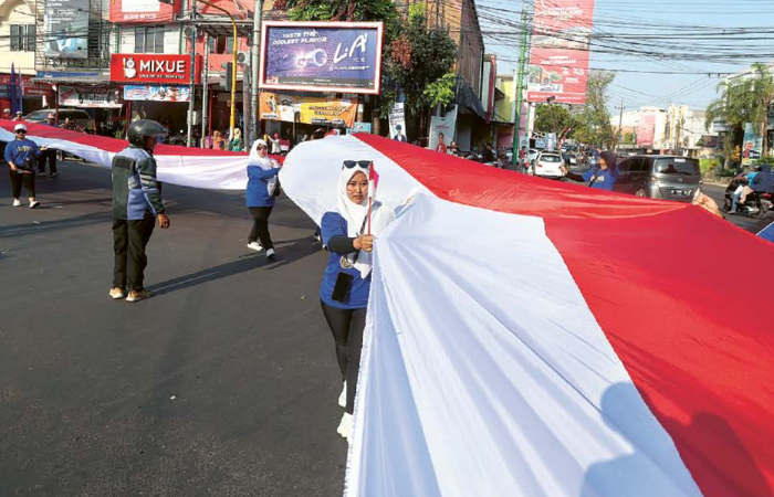 KARNAVAL KEBANGSAAN: Warga Kelurahan Karangbesuki, Kecamatan Sukun membentangkan bendera sepanjang 79 meter sambil berjalan pada acara karnaval kemarin. foto kiri, salah seorang peserta karnaval dari