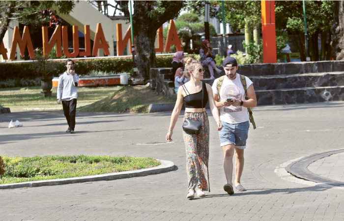 SENANG JALAN-JALAN: Dua wisatawan mancanegara berjalan menikmati suasana Alun-Alun Merdeka kemarin siang.