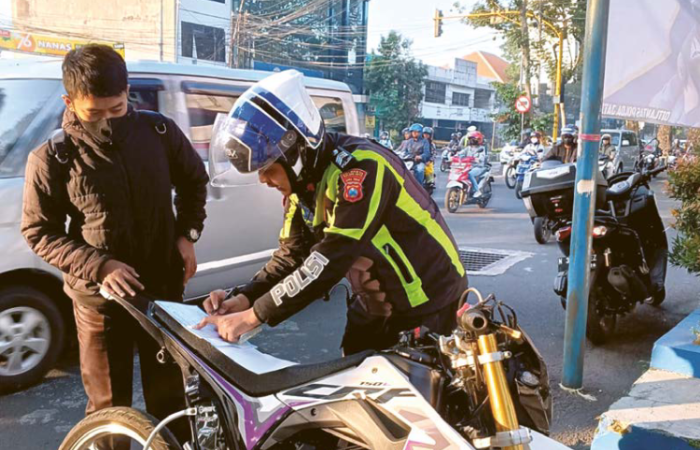 MENGGANGGU: Personel Satlantas Polresta Malang Kota menilang satu pengendara sepeda motor yang memakai knalpot brong di simpang empat Kaliurang bulan lalu.