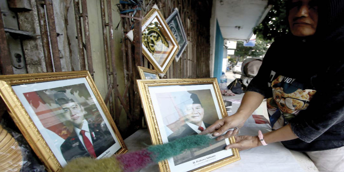 BANYAK DICARI: Seorang pedagang di Pasar Besar Malang membersihkan foto Prabowo-Gibran sebelum dijual ke pembeli kemarin siang.