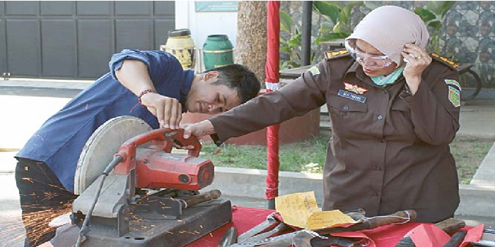 PAKAI GERINDA: Alfi Zuhroh SH, Jaksa Fungsional Kejari Kabupaten Malang (kanan) ikut memusnahkan barang bukti senjata tajam, kemarin. (KEJARI KABUPATEN MALANG FOR RADAR KANJURUHAN)