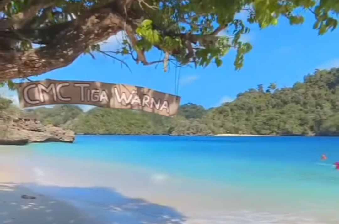 Logo CMC Tiga Warna tergantung di pohon di pinggir pantai