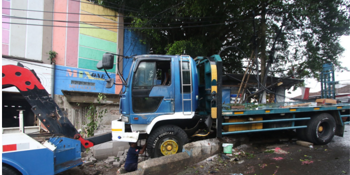 AKIBAT REM BLONG: Mekanik kendaraan derek memasang besi pengait ke truk Hino yang menabrak pagar tembok di Jalan Apel, Kecamatan Dau, Kota Batu, kemarin (10/12).
