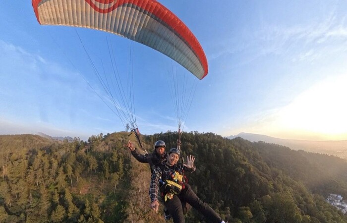 Wisatawan sedang paralayang sambil menikmati keindahan alam di Kota Batu