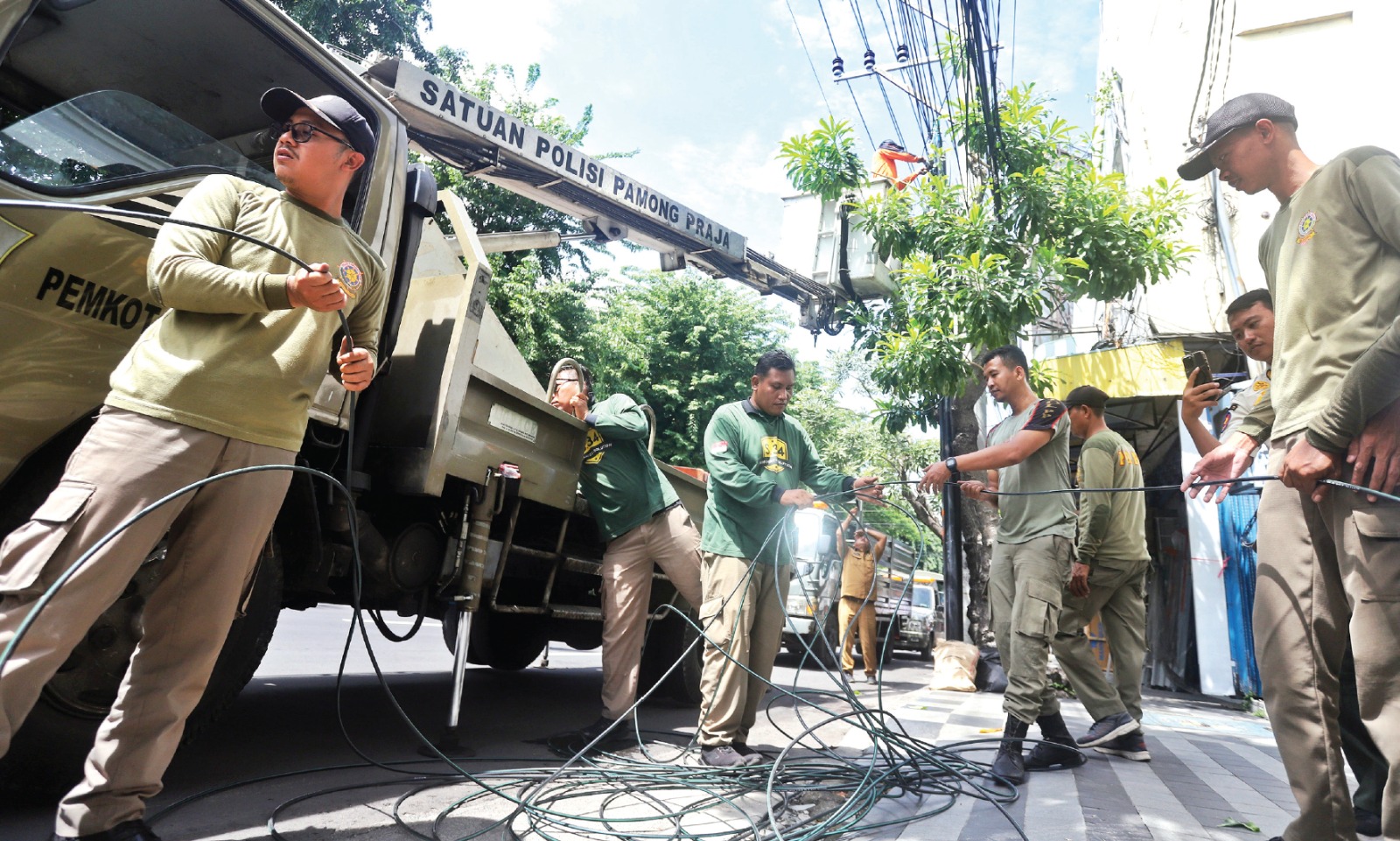 MELANGGAR ATURAN: Petugas Satpol PP Surabaya menyita kabel jaringan utilitas milik provider yang tak membayar sewa sejak 2021 kemarin siang. (AKHMAD KHUSAINI/JAWA POS)