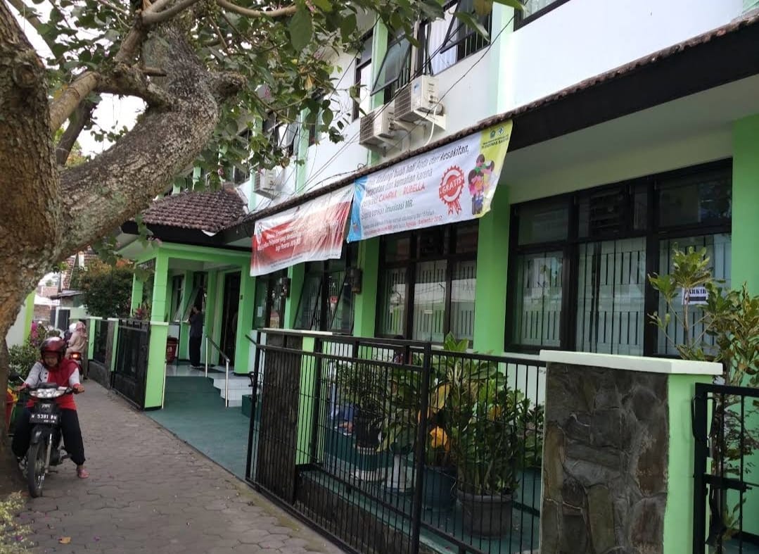 Seorang ibu-ibu bermotor lewat depan Puskemas Bareng Kota Malang. (Google: Rudy Kurniawan)