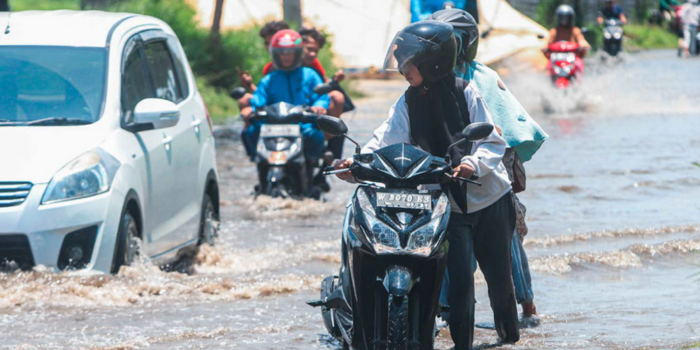 KENA BANJIR: Seorang pengendara sepeda motor mendorong kendaraannya yang mogok di area menuju Stadion GBT kemarin.