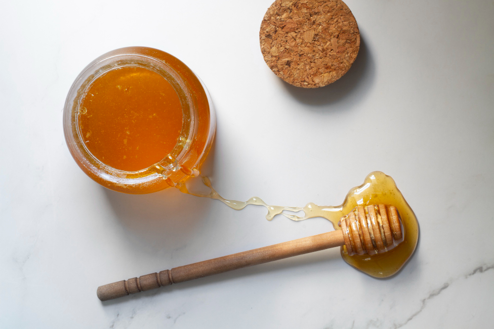 Top view of jar of honey with honey dipper (Freepik)