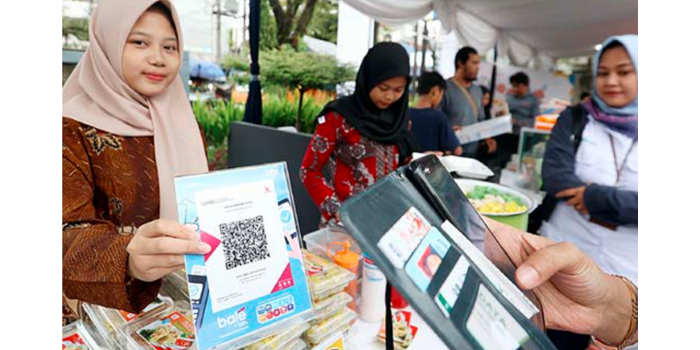 TERUS MENINGKAT: Salah satu penjaga stan di pasar murah yang digelar BTN menunjukkan merchant QRIS, kemarin.