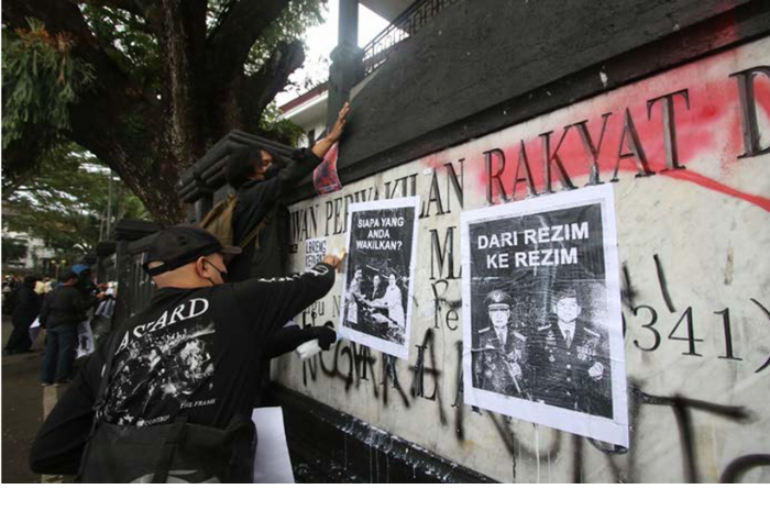 PROTES: Sejumlah demonstran memasang poster menolak UU TNI yang baru di pagar tembok gedung DPRD Kota Malang kemarin. (SATRIA CAHYONO/RADAR MALANG)