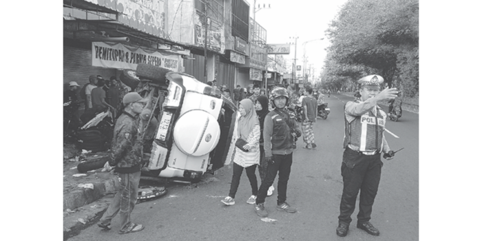 Personel Satlantas Polres Malang mengatur arus lalu lintas di jalan raya Panglima Sudirman, Kecamatan Singosari, sementara mobil Daihatsu terios yang terbalik masih berada di lokasi kejadian.