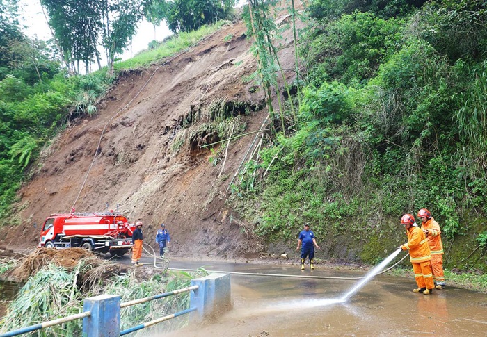 BUTUH WAKTU LAMA: Tim Damkarmat Kota Batu membersihkan badan Jalan Pura Arjuno di Desa Tulungrejo, Kecamatan Bumiaji, menggunakan air setelah material longsoran berhasil disingkirkan kemarin (20/5).