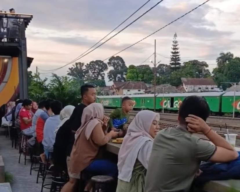 Seorang penumpang kereta menikmati kopi sambil bersantai di kafe dekat Stasiun Kota Baru Malang. Lokasi strategis jadi pilihan favorit transit.