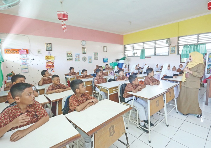 MENYIMAK: Guru kelas salah satu SD negeri di Surabaya memberikan penjelasan materi pelajaran kepada siswa.