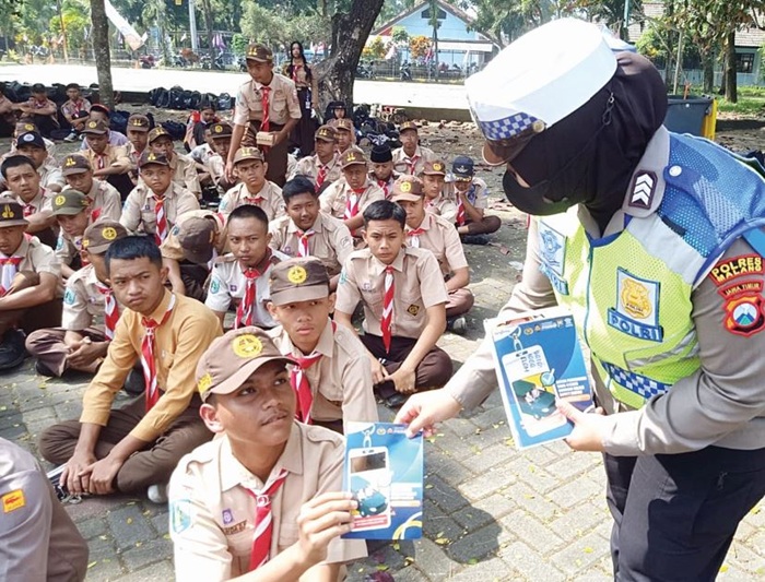 EDUKASI: Personel Satlantas Polres Malang membagikan selebaran aturan berlalu lintas di SMKN 1 Singosari.