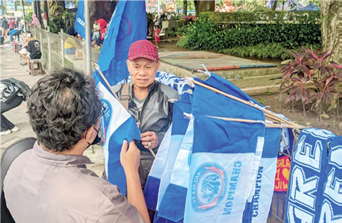 MEMANFAATKAN MOMEN: Penjual atribut Arema membuka lapak di sekitar Stasiun Malang kemarin sore.