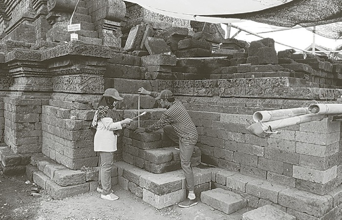 PENINGGALAN KERAJAA N: Seorang pekerja mengukur bebatuan untuk memudahkan pemasangan bebatuan kemarin (28/8). Pemugaran Candi Jago, Dusun Jago, Desa Tumpang, Kecamatan Tumpang dilakukan melalui tiga t