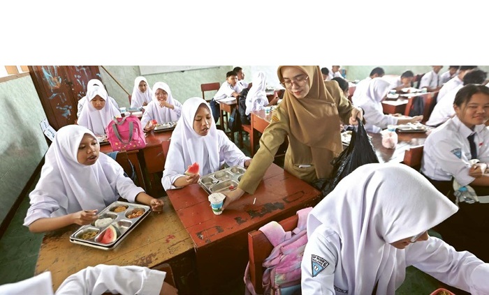 PERLUAS JANGKAUAN: Salah satu guru di SMPN 6 Kota Malang membagikan paket makan bergizi gratis (MBG), kemarin.