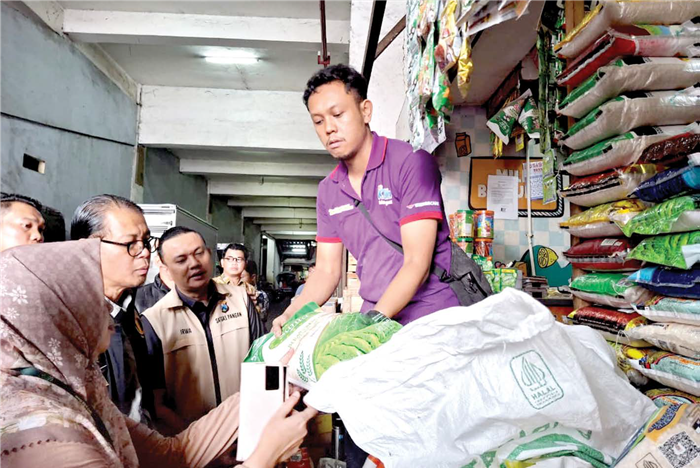 TEMUI BANYAK CATATAN: Seorang pedagang Pasar Dinoyo menunjukkan beras kemasan 5 kg kepada petugas Satgas Pengendalian Harga Beras Tahun 2025 kemarin.