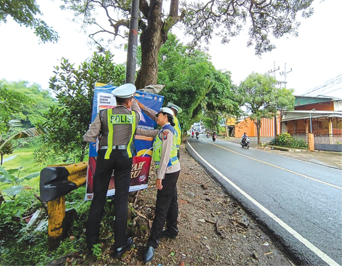 ANTISIPASI LAKA: Personel Satlantas Polres Malang memasang baliho imbauan titik rawan lalu lintas di jalur utama Karangploso menuju Kota Batu kemarin.