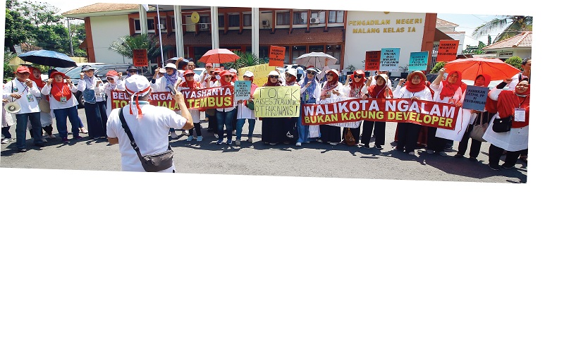 SIDANG PERDANA: Puluhan warga RW 12 Kelurahan Mojolangu, Lowokwaru membentangkan banner bernada kecaman di depan Pengadilan Negeri (PN) Malang.