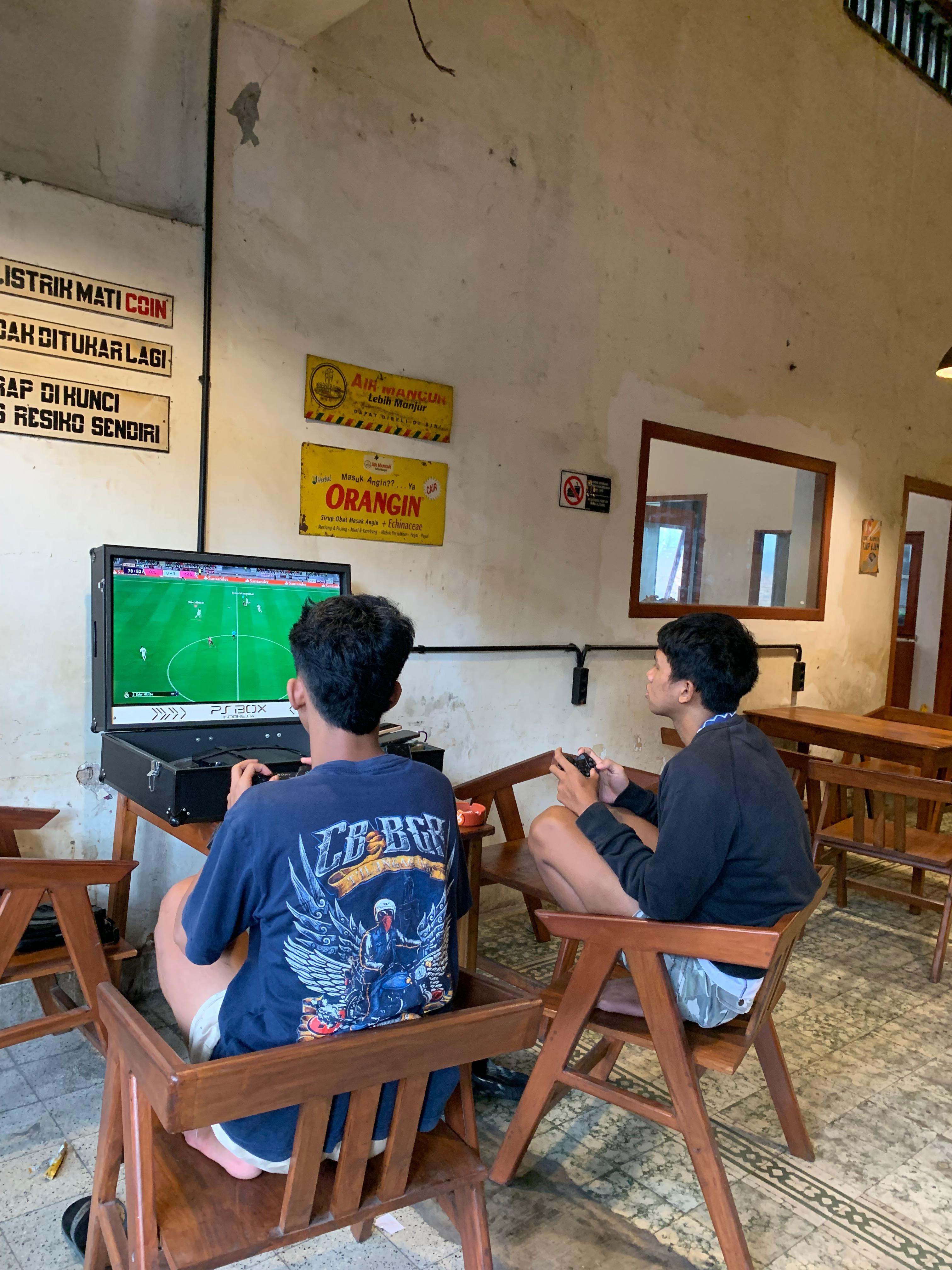 SERU: dua pemuda bermain E-Football  menggunakan playbox di sebuah kafe.  Perangkat yang lebih ringkas dan  mudah dibawa ke mana-mana jadi  alasan anak muda menggemarinya.