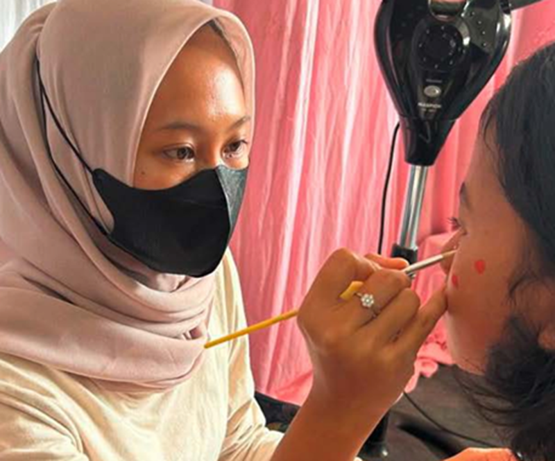 TELATEN: Face painter melukis wajah seorang remaja menggunakan cat khusus.