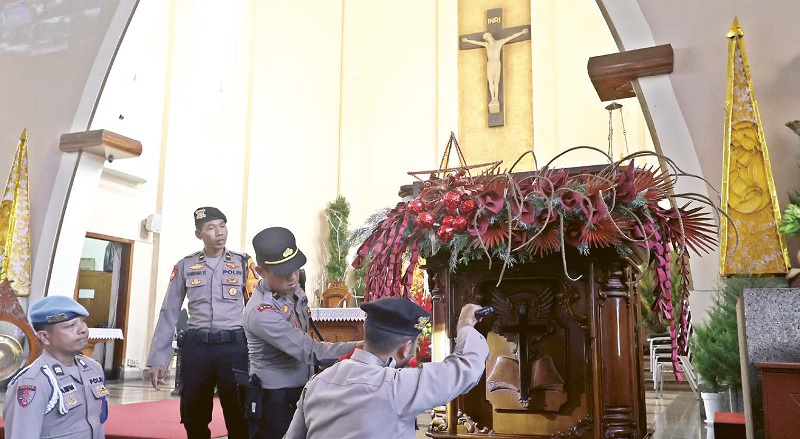 LINDUNGI UMAT: Beberapa personel polisi menyisir sejumlah area di gereja kemarin (24/12). Petugas melakukan sterilisasi agar umat Kristiani dapat menjalankan ibadah Natal dengan rasa aman