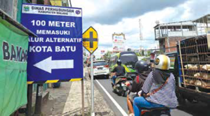 LANGGANAN MACET: Banner penanda untuk jalur alternatif sudah dipasang petugas untuk pengendara yang terjebak kemacetan di simpang lima Kepuharjo, Karangploso.