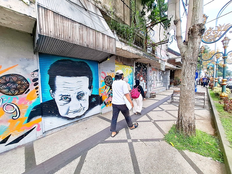 SIMPAN CERITA MENARIK: Warga melintas di kawasan Kajoetangan Heritage dengan latar mural Arifin atau Mbah Gombloh di dinding pertokoan, kemarin (27/1).