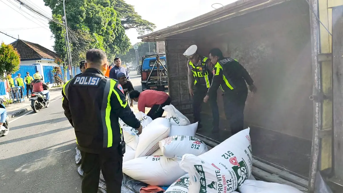 SEMPAT BIKIN MACET: Polisi ikut membantu memindahkan muatan pakan ternak dari truk yang terguling di Jalan Jenderal Ahmad Yani, Blimbing, kemarin pagi (3/4). (SATLANTAS POLRESTA MAKOTA FOR RADAR MALANG)