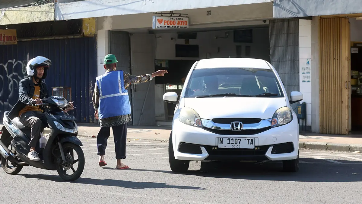 WAJIB PAKAI ROMPI: Salah satu jukir memberi aba-aba kepada salah satu pengemudi mobil di Jalan Pasar Besar, kemarin. (Darmono / Radar Malang)