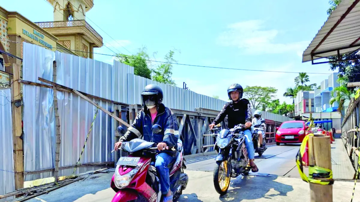 MELEWATI JEMBATAN DARURAT: Sejumlah pengendara roda dua melewati jembatan bailey akibat jembatan Sonokembang belum rampung diperbaiki. Pihak DPUPRPKP Kota Malang pengecoran melakukan pengecoran abutment. (Foto: Nabila Amelia)