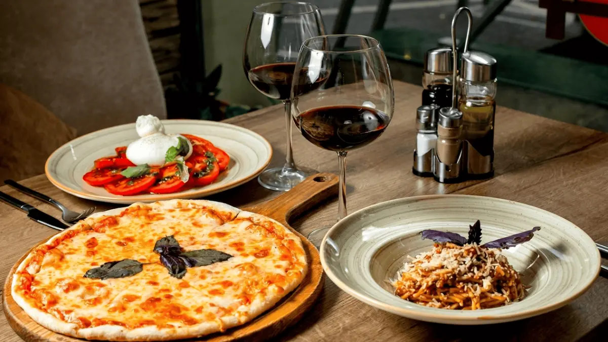 Jamuan makan malam yang menyajikan piza Margherita, pasta Bolognese, salad Burrata, dan dua gelas anggur merah. (Freepik / Google)