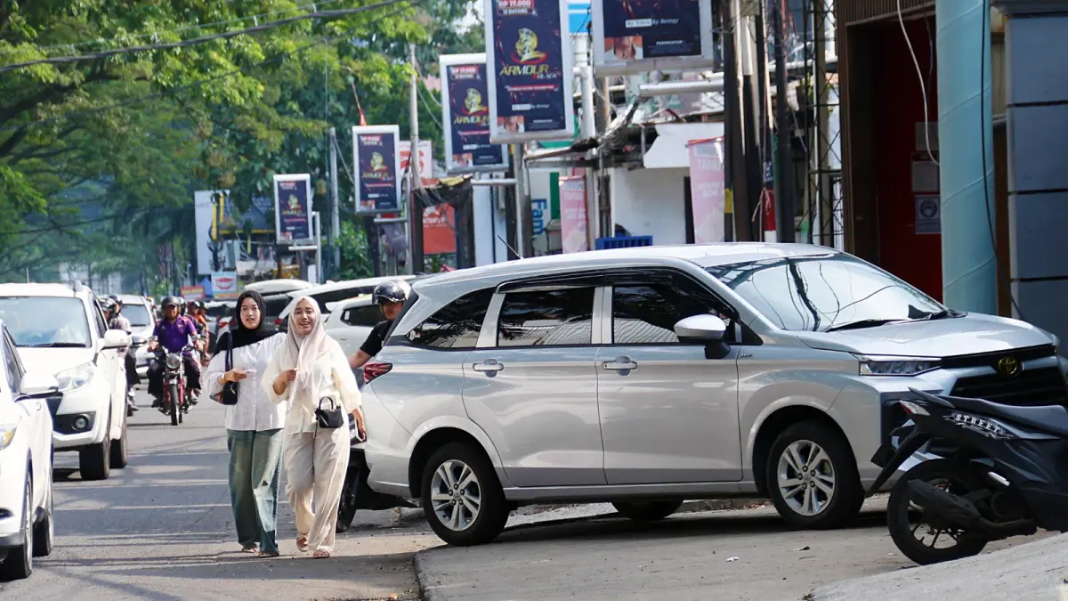 HARUS DITERTIBKAN: Dua pejalan kaki terpaksa melintasi bahu jalan karena trotoar di Jalan Soekarno-Hatta dipakai parkir kendaraan roda empat kemarin