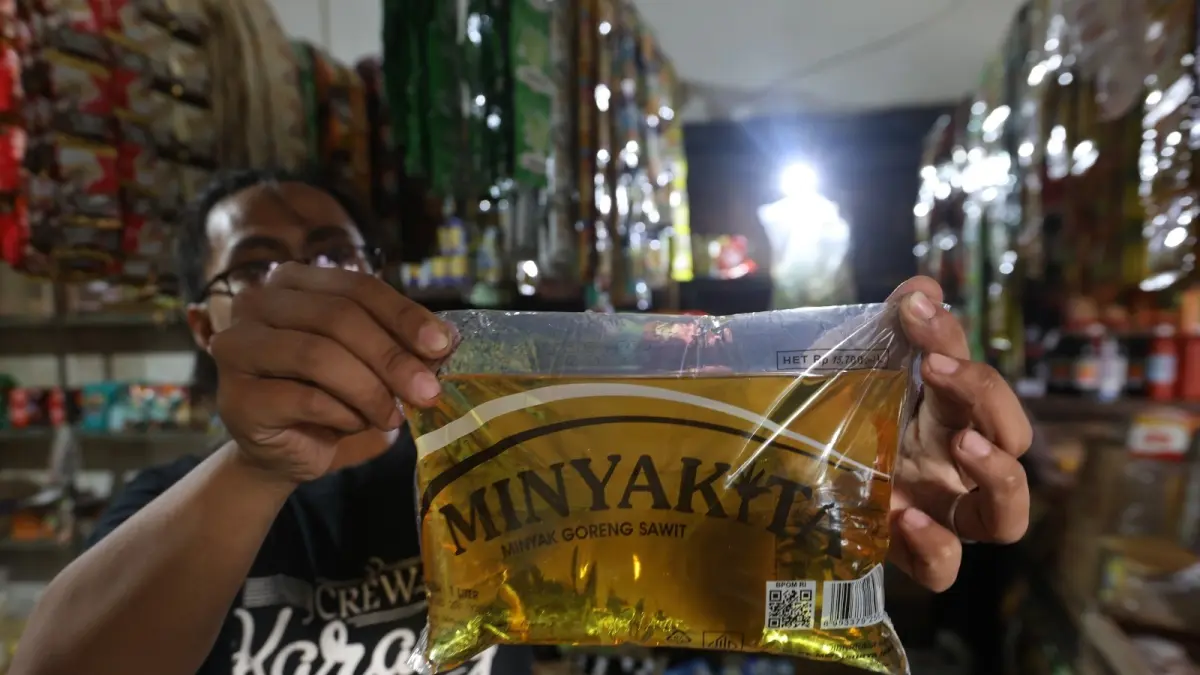 EFEK EKONOMI GLOBAL: Seorang pedagang di Pasar Kebalen Kota Malang, menunjukkan salah satu produk minyak goreng yang dijual di tempatnya, kemarin. (Foto:Darmono)
